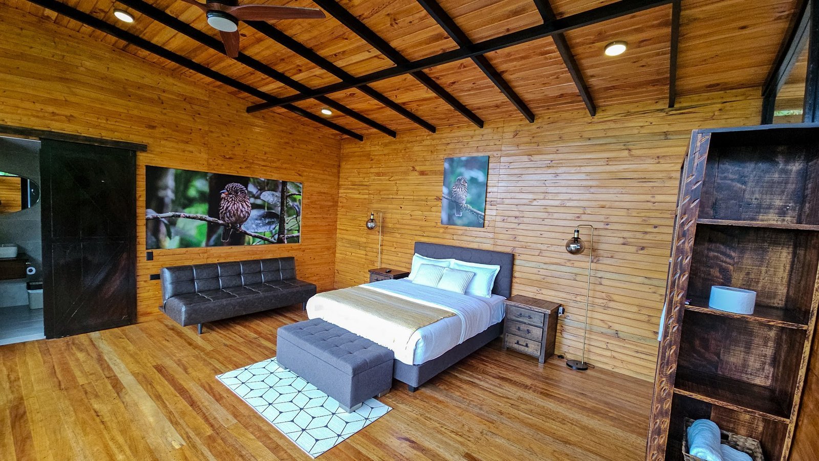 Habitación de Buglas con paredes de madera, cama doble, sofá y fotografías de aves