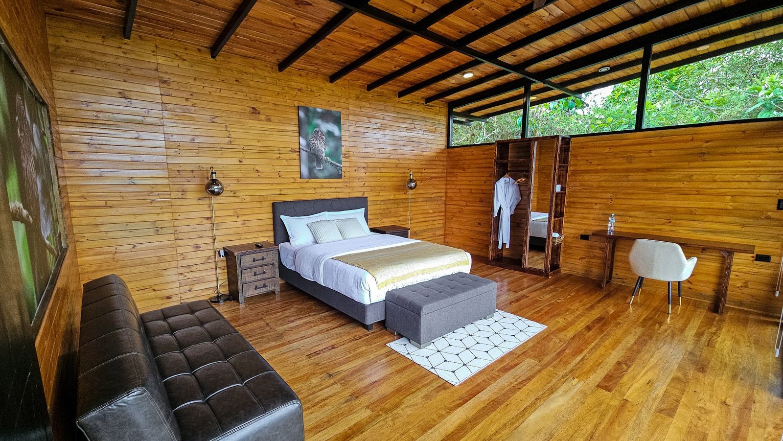 Habitación de Buglas con cama doble, sofá, escritorio y vista a la vegetación